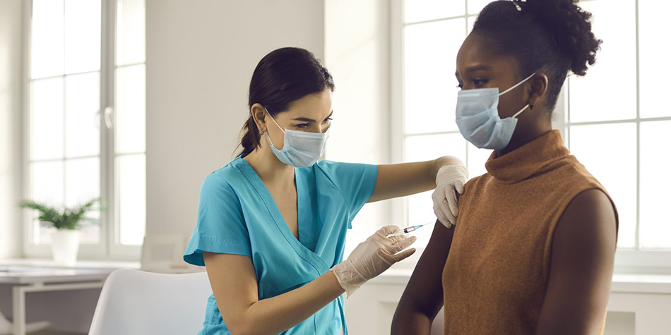 A woman wearing a face mask receives the COVID vaccine from a medical professional.